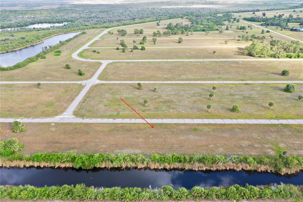 An aerial view shows a vacant, grassy residential lot situated between a paved road and a canal — 12319 GREENLING WAY, PLACIDA, FL