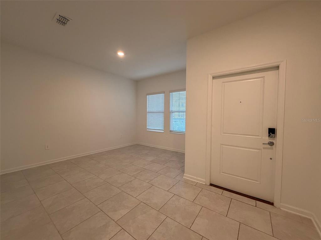 An empty room with light-colored tile flooring, white walls, and a white front door — 2165 SWEET HONEY LANE, APOPKA, FL