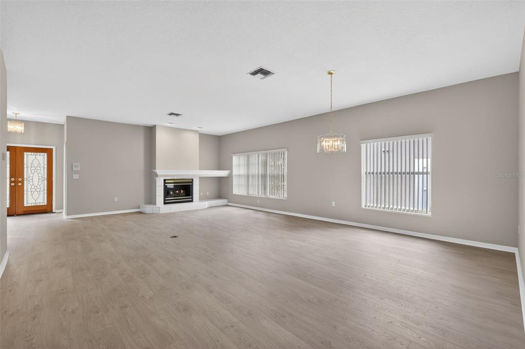A spacious living room features light wood-look flooring, a fireplace, and two large windows — 4856 WESTCHESTER COURT, OLDSMAR, FL