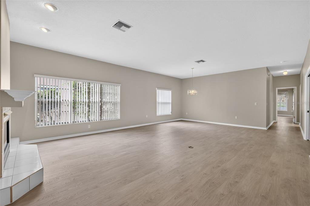 An empty living room features light wood-look flooring, beige walls, and a white tile fireplace — 4856 WESTCHESTER COURT, OLDSMAR, FL