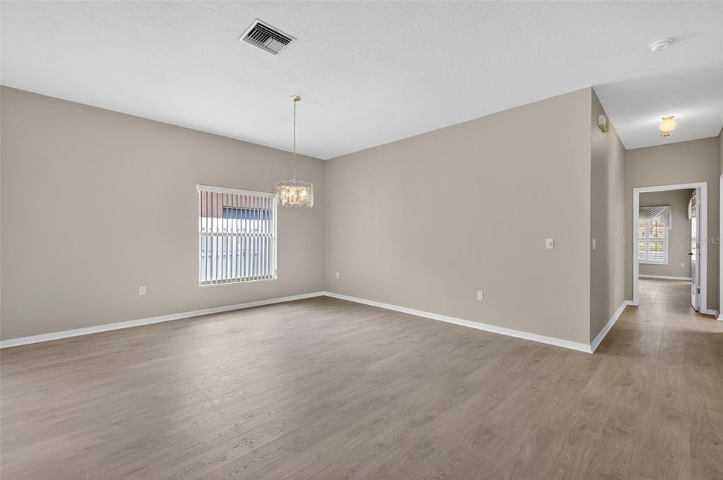 An empty dining room with light wood-look flooring, a crystal chandelier, and a single window — 4856 WESTCHESTER COURT, OLDSMAR, FL