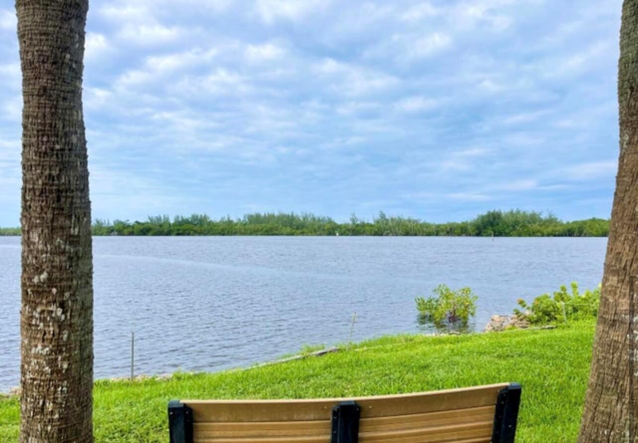 A wooden bench sits on a grassy lawn overlooking a calm body of water — 6142 SE Landing Way # 11, Stuart FL 34997, STUART, FL