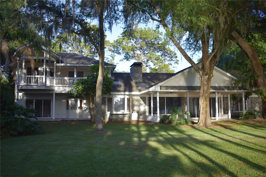 The rear exterior of a two-story house features a stone chimney, balcony, and covered patio — 16308 ROCK LAKE DRIVE, ODESSA, FL
