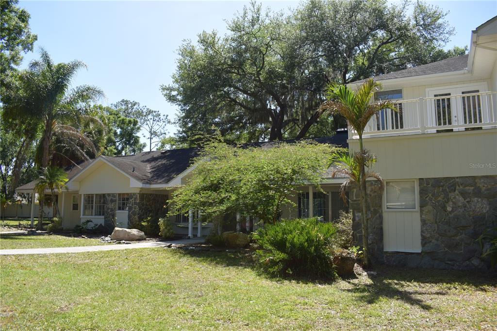 A two-story house with stone siding and a balcony stands among trees and grass — 16308 ROCK LAKE DRIVE, ODESSA, FL