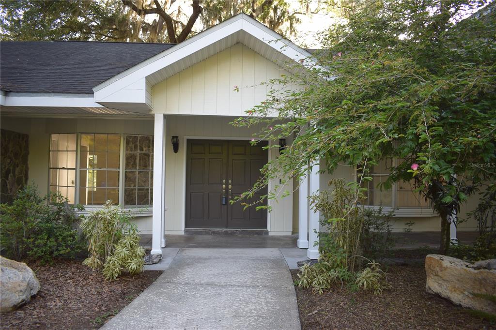 A concrete walkway leads to the double front doors of a house with yellow siding — 16308 ROCK LAKE DRIVE, ODESSA, FL