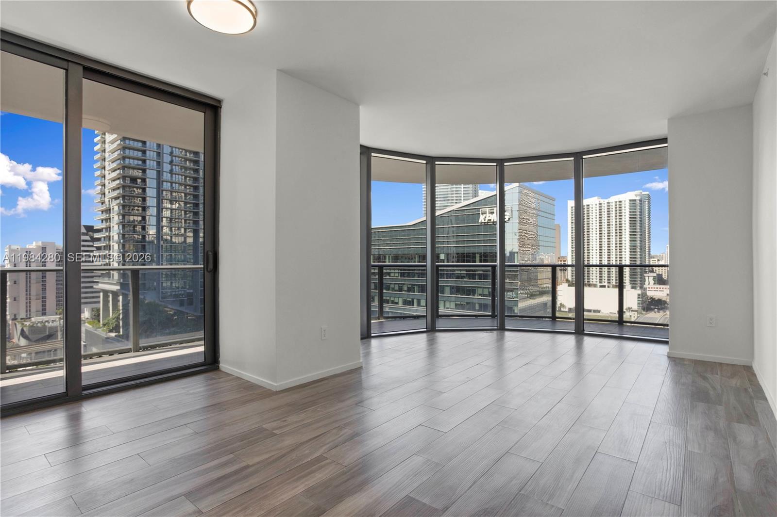 An empty room with wood-look flooring, white walls, and floor-to-ceiling windows overlooking city buildings — 801 S Miami Ave # 1609, Miami FL 33130, MIAMI, FL