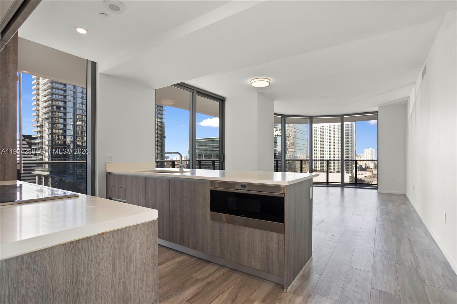 A modern kitchen with wood-grain cabinetry and white countertops overlooks a bright living area — 801 S Miami Ave # 1609, Miami FL 33130, MIAMI, FL