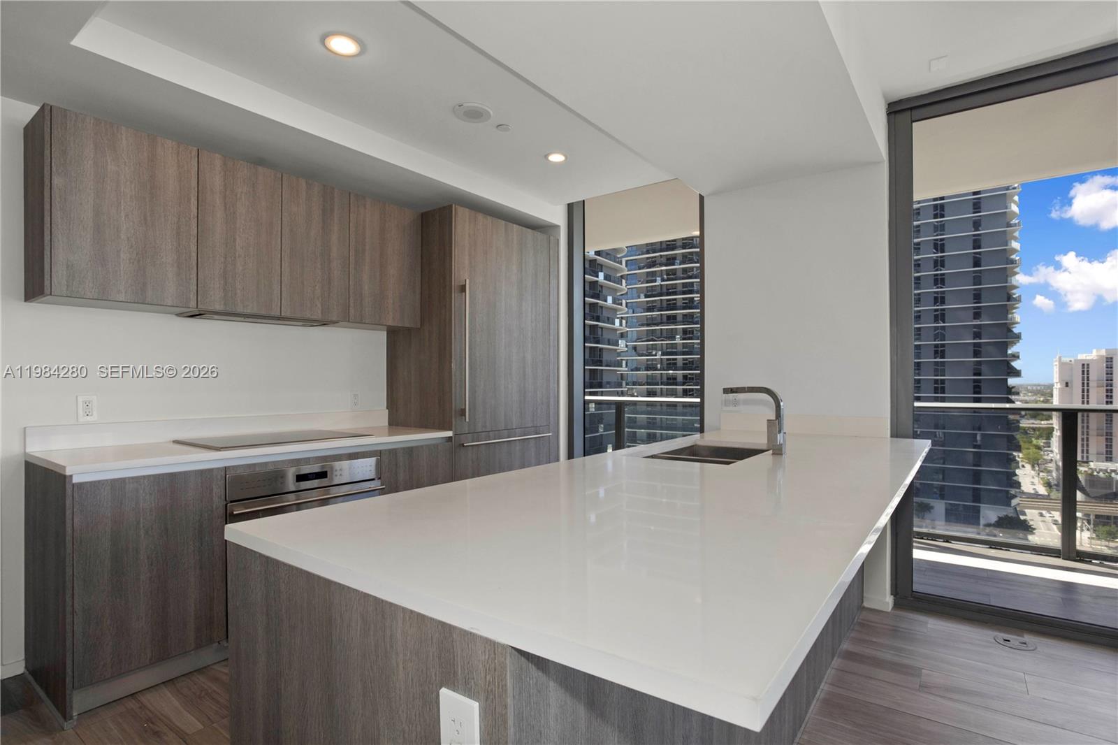 A modern kitchen features wood-grain cabinetry, white countertops, and a large island with a sink — 801 S Miami Ave # 1609, Miami FL 33130, MIAMI, FL