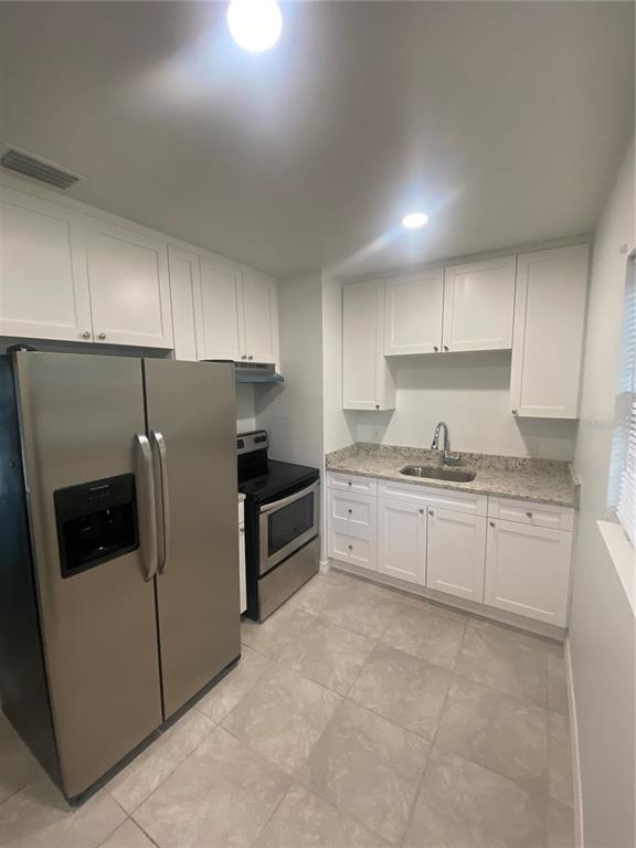 A kitchen features white cabinets, stainless steel appliances, granite countertops, and light-colored tile flooring — 7020 BAYWOOD DRIVE, TAMPA, FL