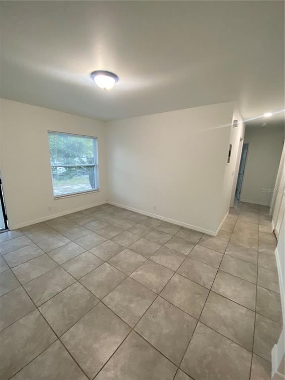 An empty room with light-colored tile flooring, white walls, and a single window — 7020 BAYWOOD DRIVE, TAMPA, FL