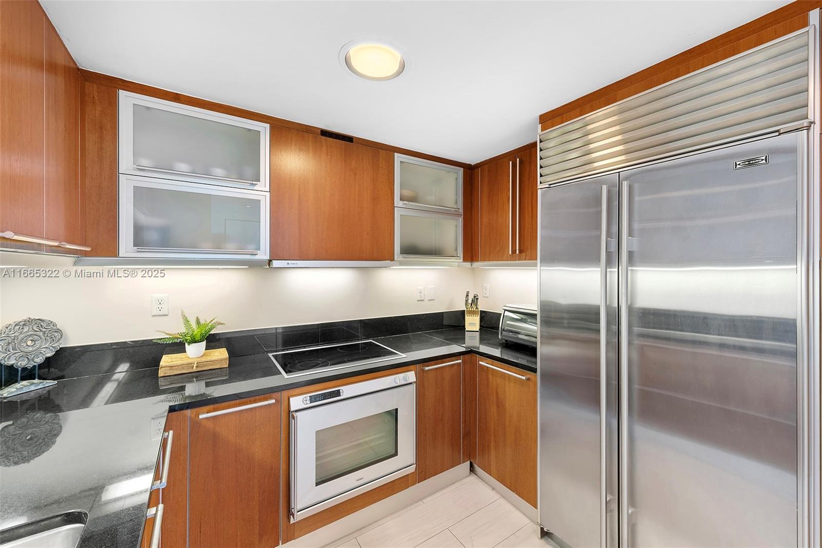 A kitchen features wood cabinets, black countertops, stainless steel appliances, and a glass-front upper cabinet — 101 20th St # 2604, Miami Beach FL 33139, MIAMI BEACH, FL