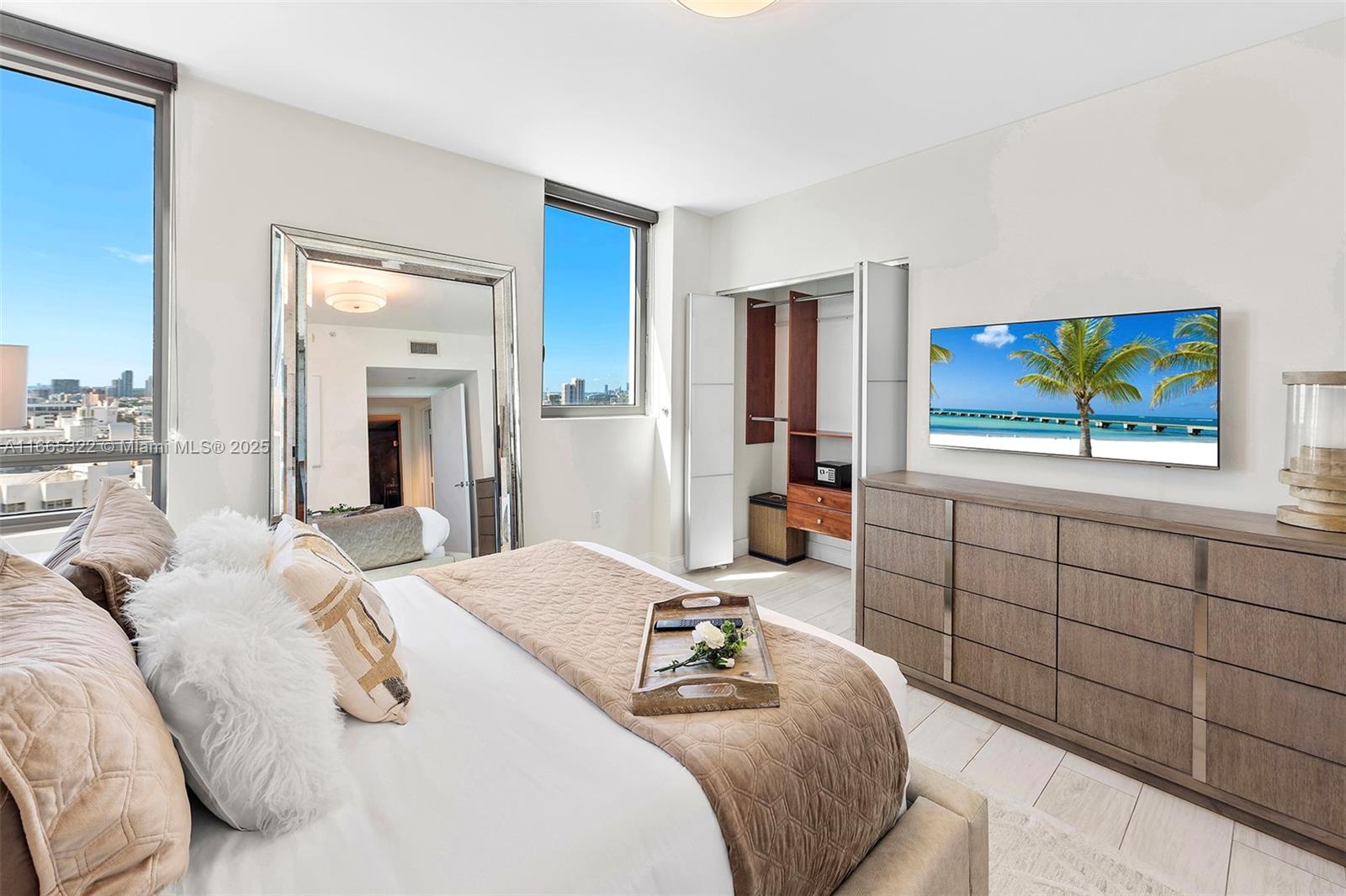 A bedroom features a bed, a large mirror, a dresser with a television, and city views — 101 20th St # 2604, Miami Beach FL 33139, MIAMI BEACH, FL