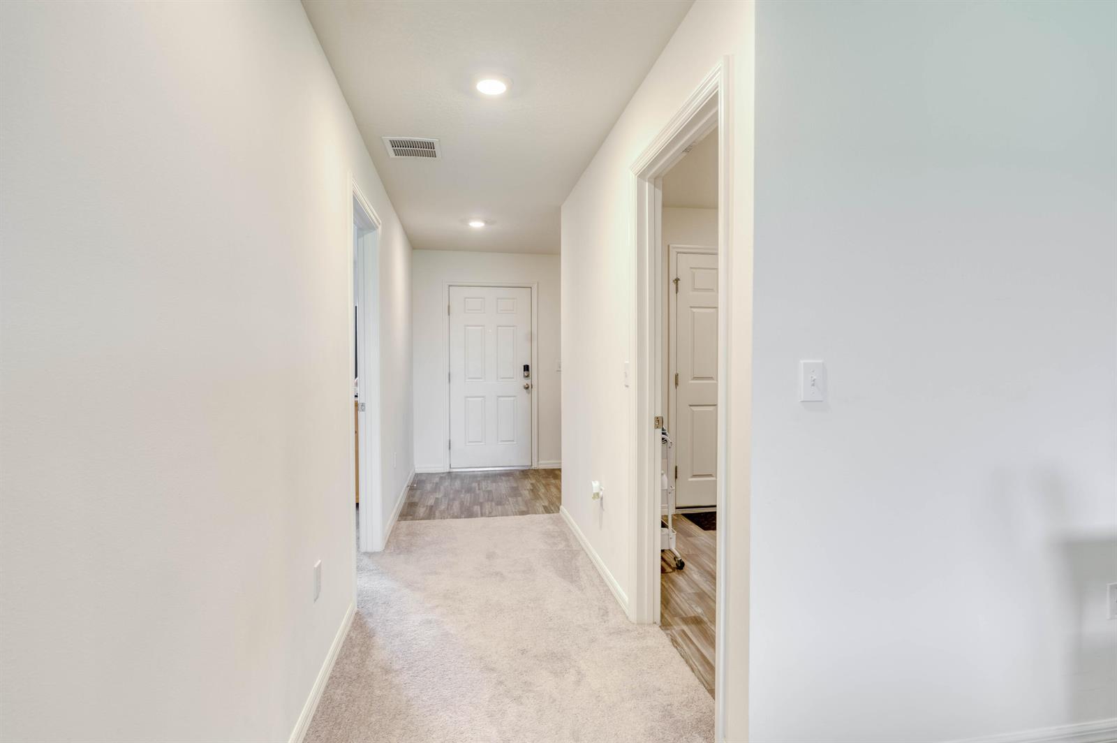 A hallway with carpeted flooring leads to a white front door with wood-look flooring — 773 SE 25TH Drive, Okeechobee FL 34974, OKEECHOBEE, FL