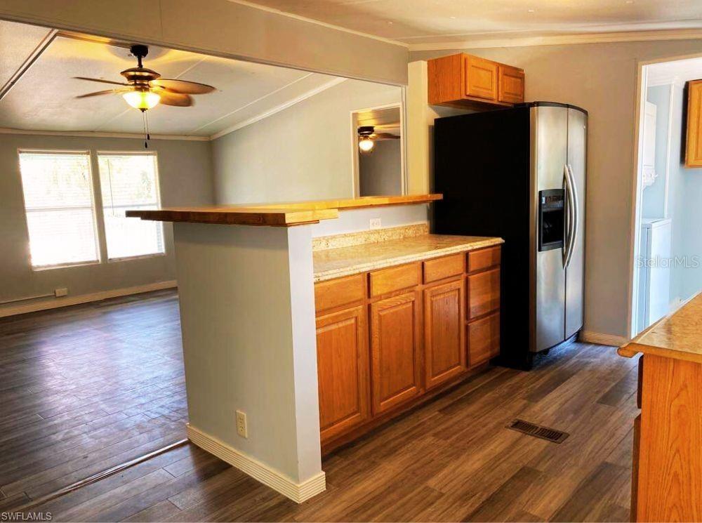 A kitchen with wood cabinets, a breakfast bar, and a black refrigerator overlooks a living area — 1281 RICHMOND AVENUE, CLEWISTON, FL