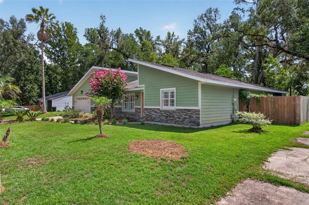 A green house with a stone facade and a slanted roof sits on a lawn — 3817 NW 28TH TERRACE, GAINESVILLE, FL