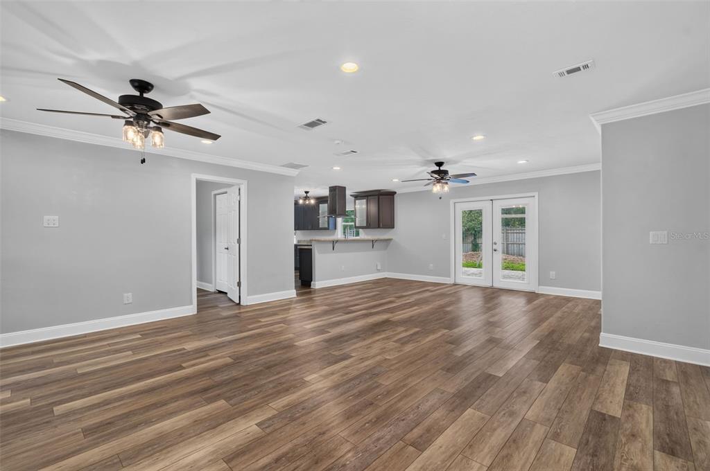An open-concept living room with wood-look flooring, two ceiling fans, and a kitchen in back — 3817 NW 28TH TERRACE, GAINESVILLE, FL