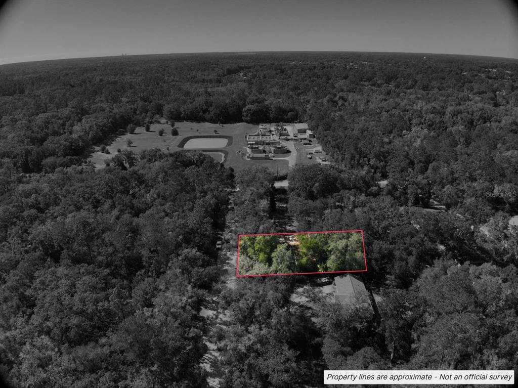 An aerial view shows a wooded lot outlined in red near a commercial facility — Lot #1 ST PATRICK DRIVE, DUNNELLON, FL
