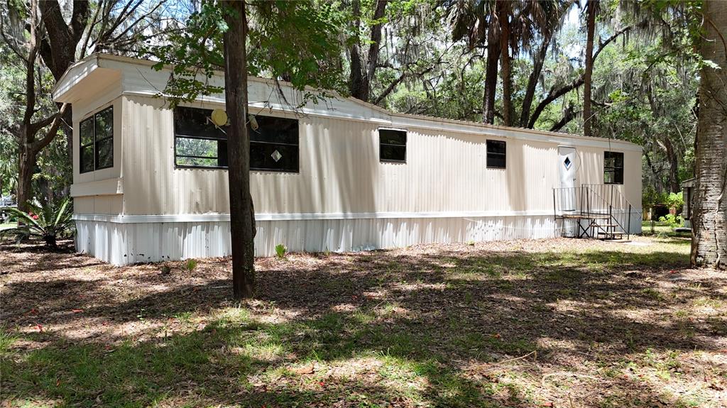 A single-wide mobile home with beige metal siding sits in a wooded, grassy lot — 11310 W YELLOW OAK LANE, CRYSTAL RIVER, FL