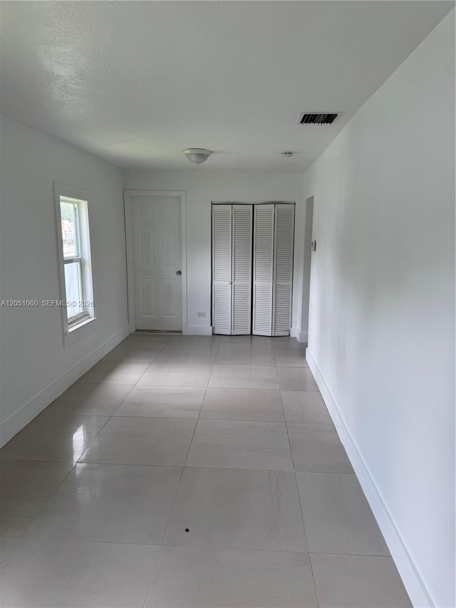 A room with white walls, light-colored tile flooring, a window, a door, and closet doors — 61 NW 53rd St, Miami FL 33127, MIAMI, FL