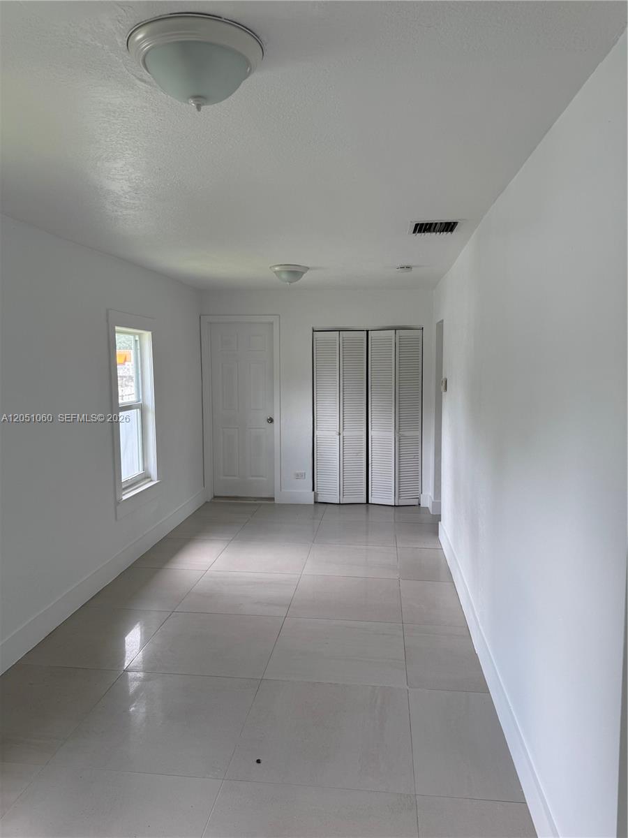 A room with white walls, light tile flooring, a window, a door, and closet doors — 61 NW 53rd St, Miami FL 33127, MIAMI, FL