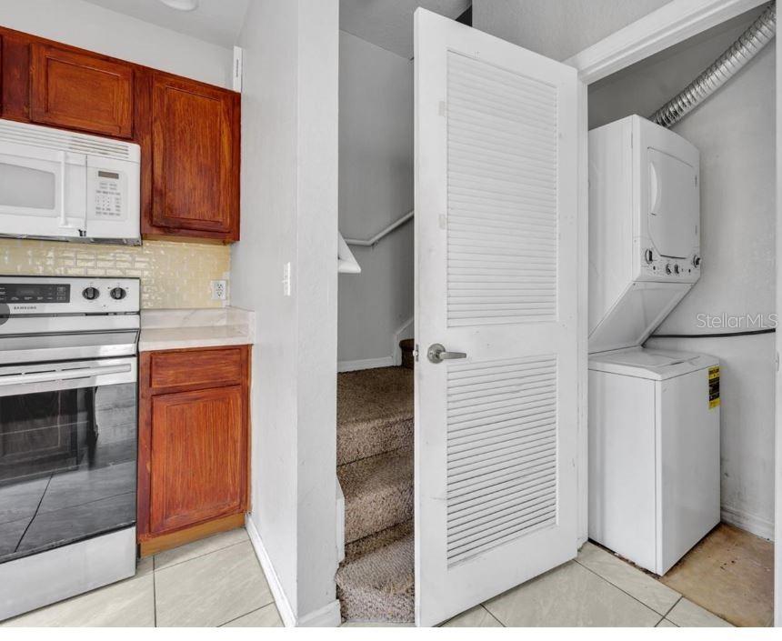 A kitchen area features wood cabinets, a white stove, a staircase, and a stacked laundry unit — 4012 SANTA MARIA DRIVE UNIT 102, KISSIMMEE, FL