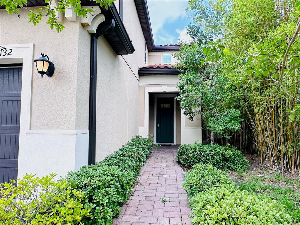 A brick walkway leads to the dark green front door of a beige stucco house — 10132 GRAND OAK CIRCLE, MADEIRA BEACH, FL