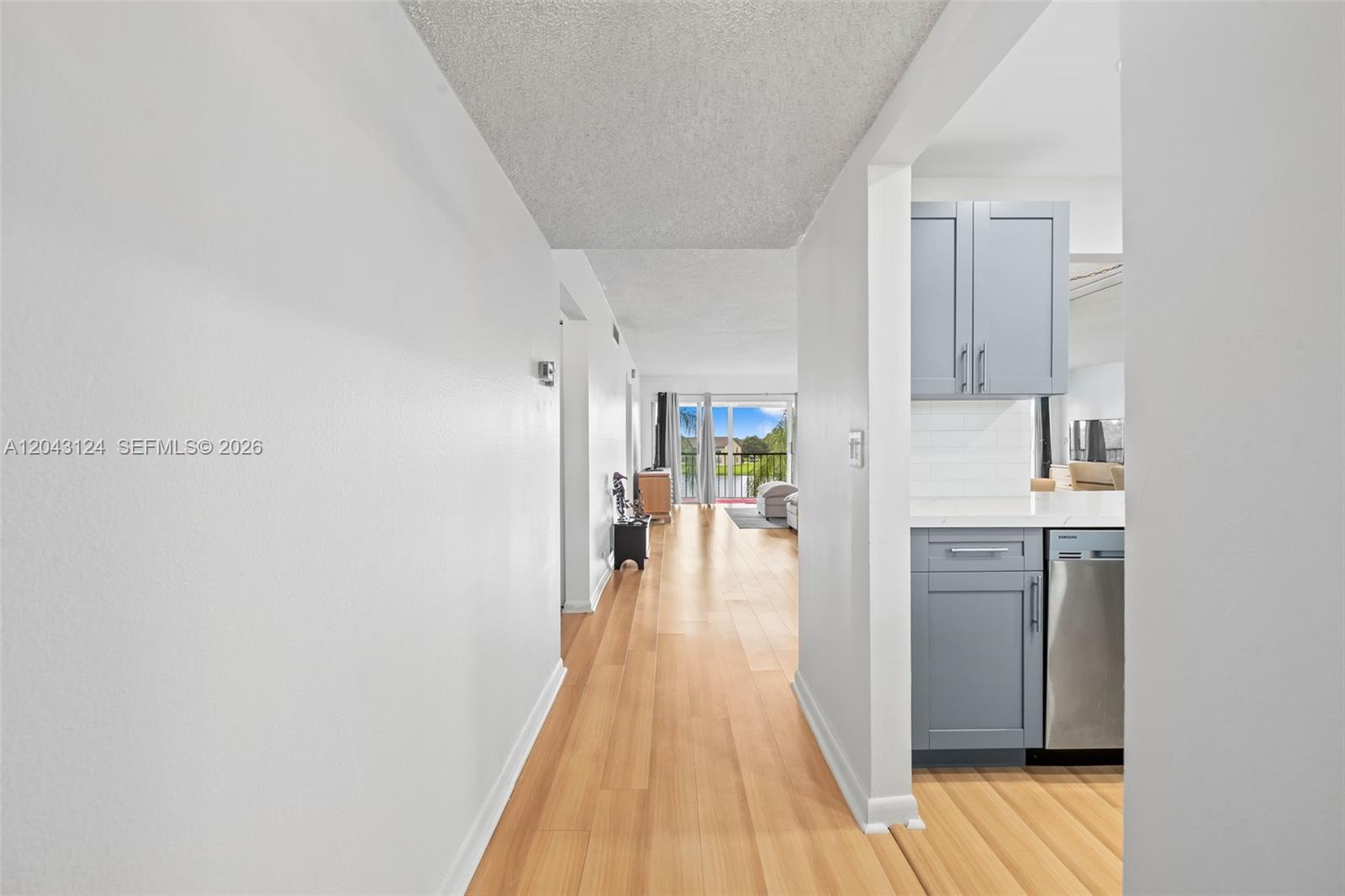 A hallway with light wood flooring leads toward a living area with a balcony view — 4025 N Nob Hill Rd # 301, Sunrise FL 33351, SUNRISE, FL