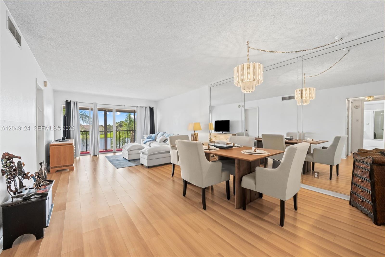 A dining area and living room with light wood floors, mirrored walls, and a balcony view — 4025 N Nob Hill Rd # 301, Sunrise FL 33351, SUNRISE, FL