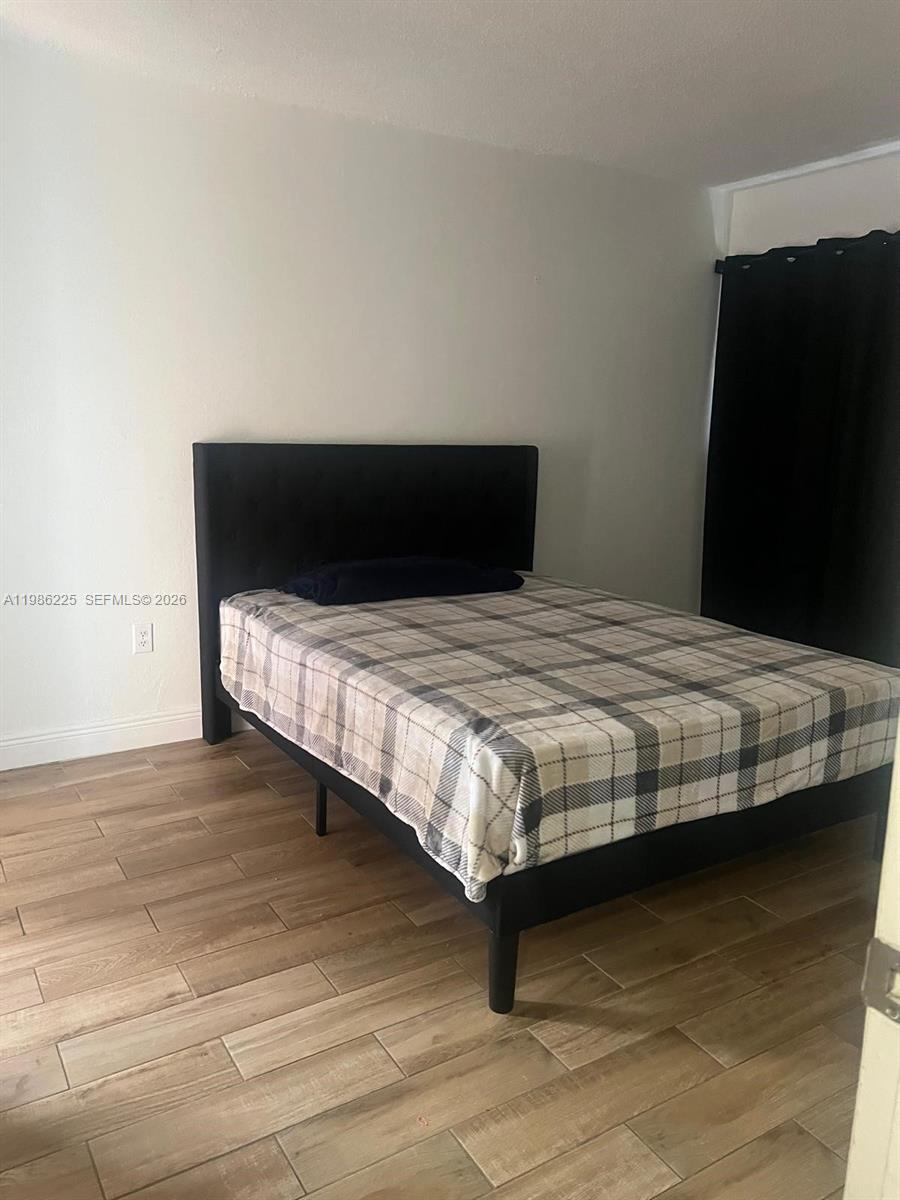 A bedroom features a black upholstered bed frame, a plaid comforter, and light wood-look flooring — 6620 W 2nd Ct # 407, Hialeah FL 33012, HIALEAH, FL