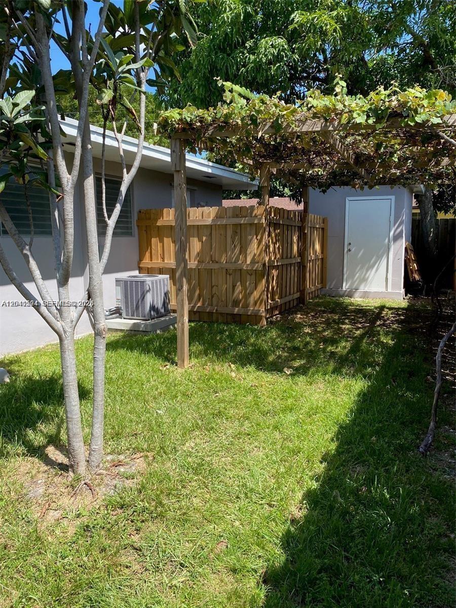A backyard features a wooden fence, a small shed, and a trellis with vines — 1005 NE 2nd St # 1, Hallandale Beach FL 33009, HALLANDALE BEACH, FL