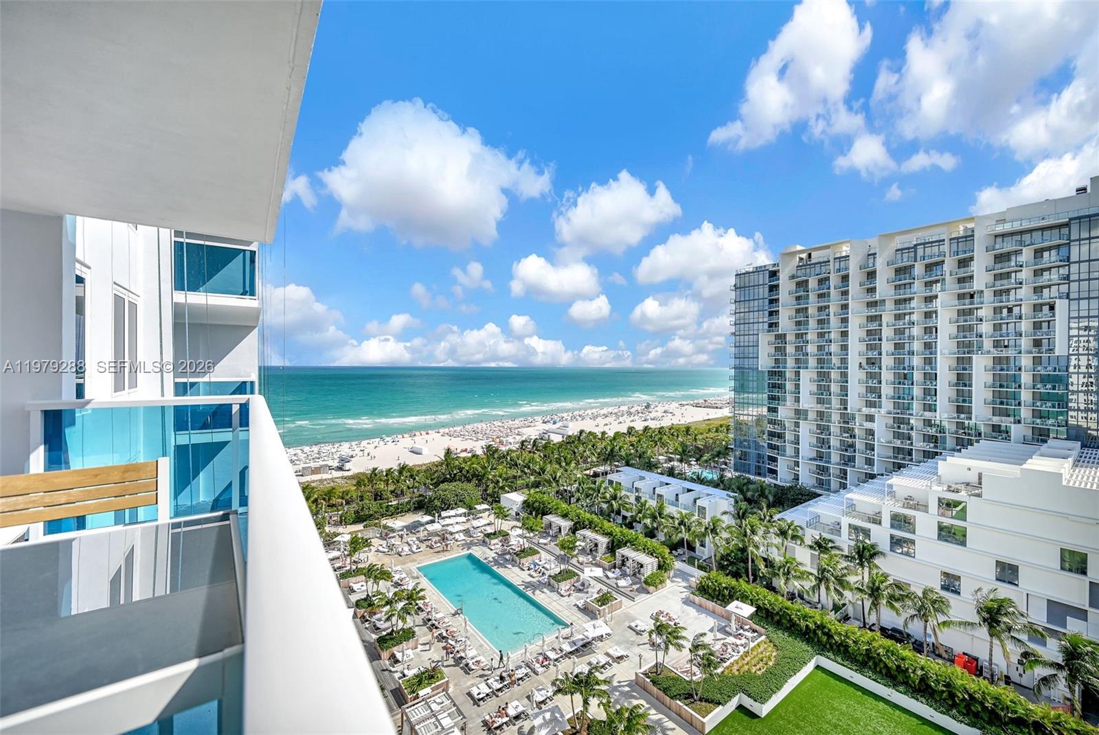 A high-angle view from a balcony overlooks a swimming pool, palm trees, and the ocean — 2301 Collins Ave # 1204, Miami Beach FL 33139, MIAMI BEACH, FL