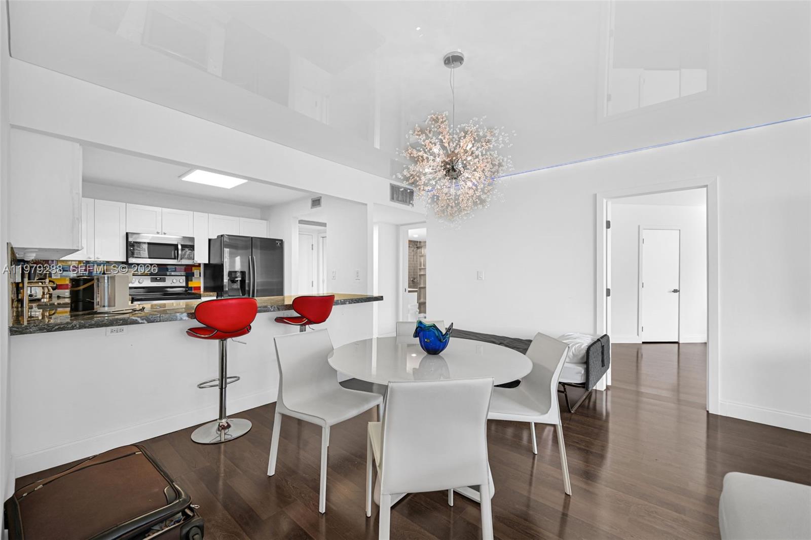 A dining area with a round table, white chairs, and a modern chandelier near a kitchen — 2301 Collins Ave # 1204, Miami Beach FL 33139, MIAMI BEACH, FL