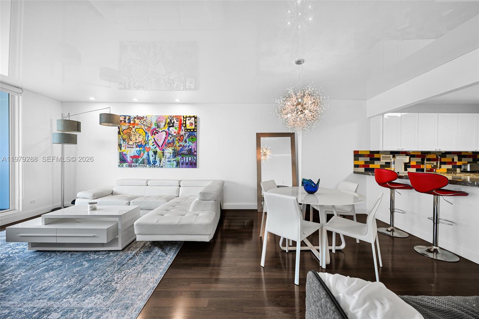 A modern living and dining area features a white sectional, colorful artwork, and dark flooring — 2301 Collins Ave # 1204, Miami Beach FL 33139, MIAMI BEACH, FL
