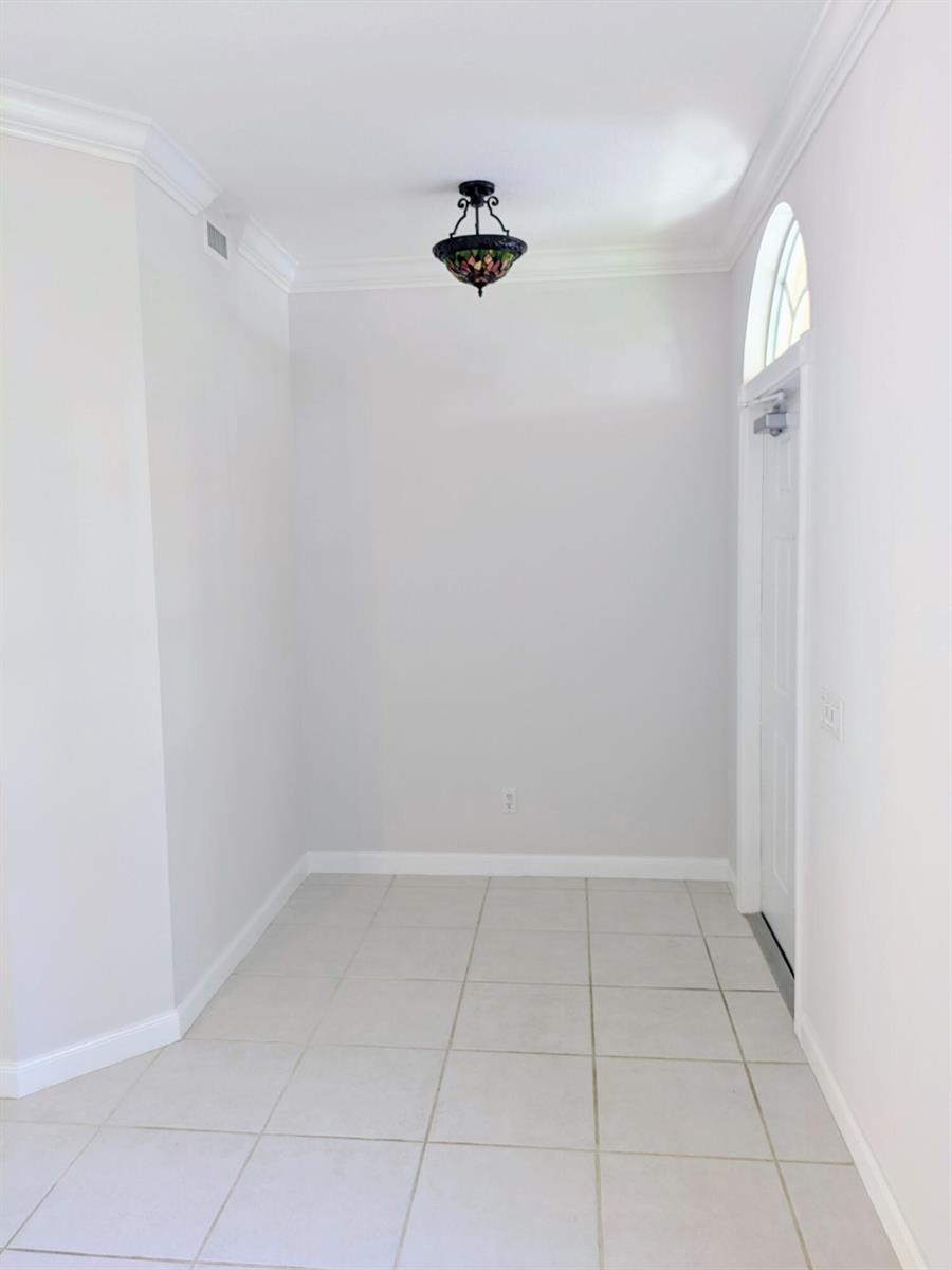 An entryway with light-colored tile flooring, white walls, crown molding, and a decorative ceiling light — 143 Middlebury Drive, Jupiter FL 33458, JUPITER, FL