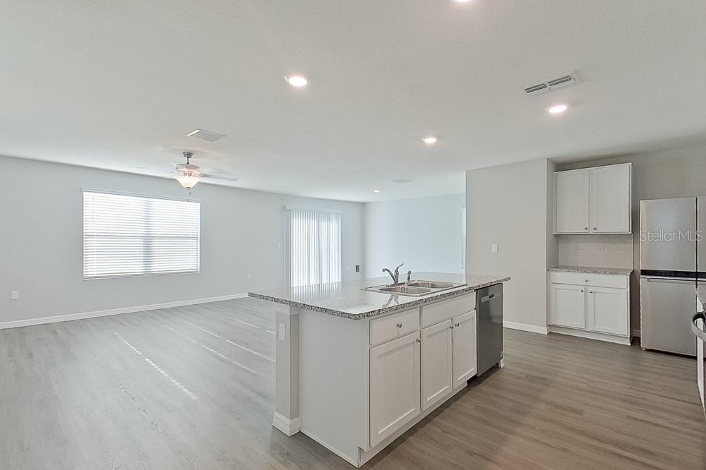 An open-concept kitchen and living area featuring white cabinets, granite countertops, and light flooring — 8614 SW 43RD TERRACE, OCALA, FL