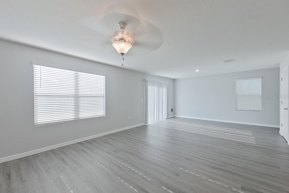 An empty living room features light gray walls, wood-look flooring, a ceiling fan, and sliding doors — 8614 SW 43RD TERRACE, OCALA, FL