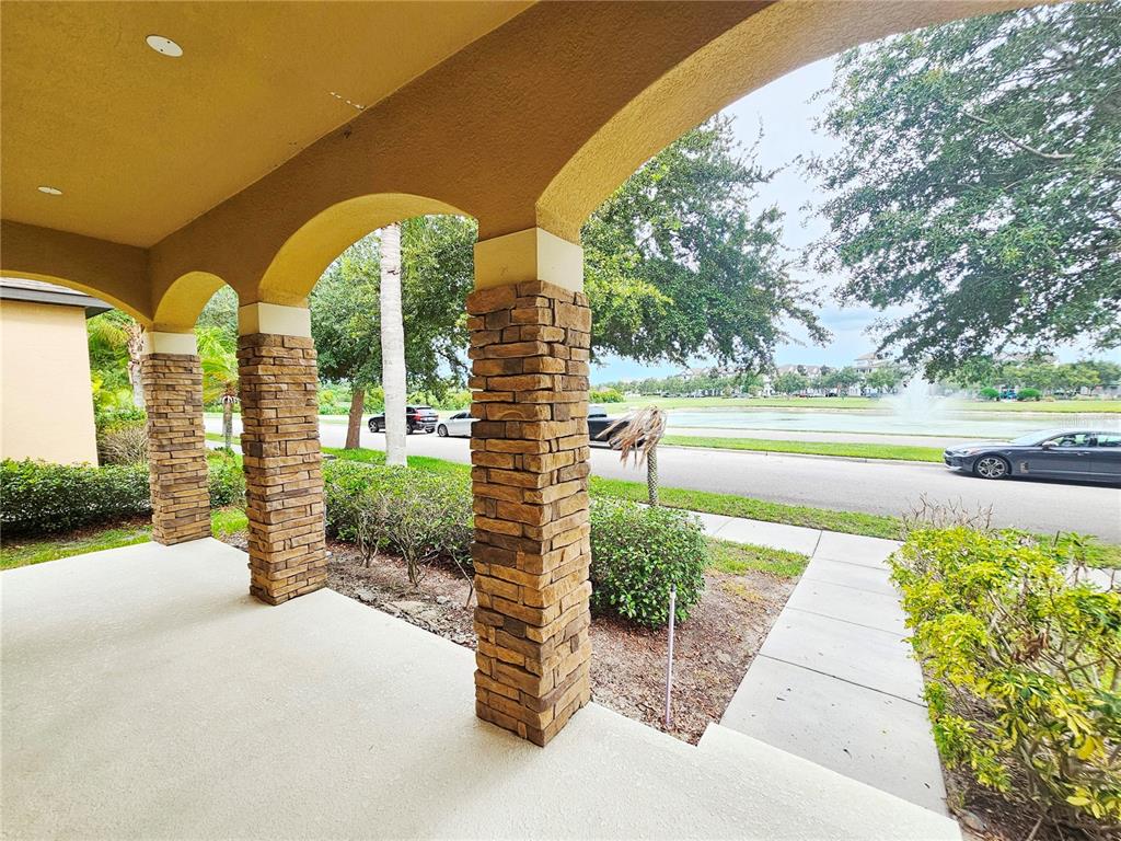 A covered porch features stone-clad pillars and arched openings overlooking a street and pond — 13778 SUMMERPORT TRAIL LOOP, WINDERMERE, FL