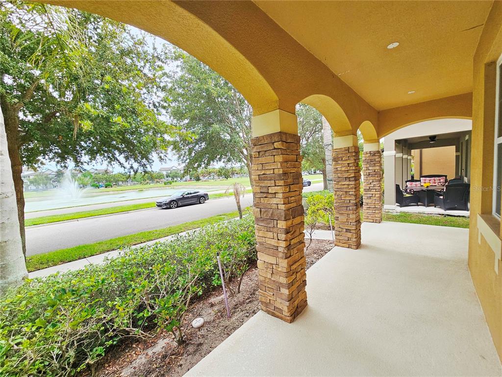 A covered porch features stone-clad columns, arched openings, and a view of a pond — 13778 SUMMERPORT TRAIL LOOP, WINDERMERE, FL