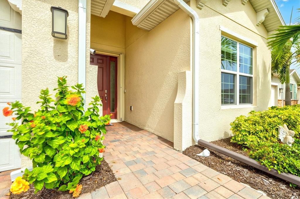 A paved walkway leads to the front entrance of a house with yellow stucco walls — 1656 REMINGTON TRACE DRIVE, PORT CHARLOTTE, FL