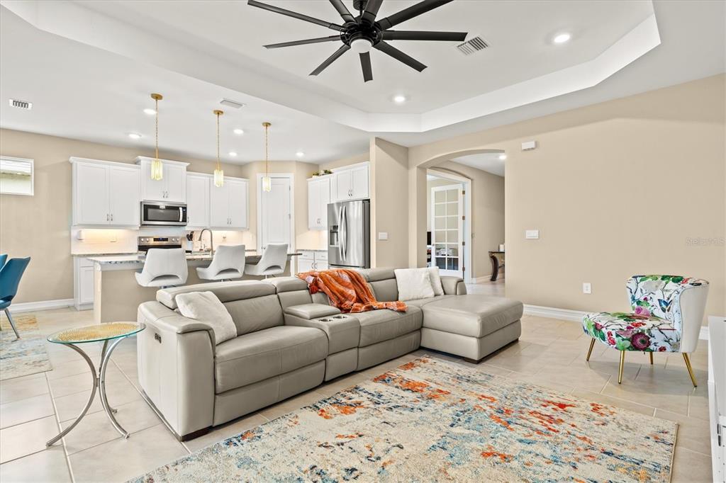 A living room with a gray sectional sofa and a floral chair opens to a kitchen — 1656 REMINGTON TRACE DRIVE, PORT CHARLOTTE, FL