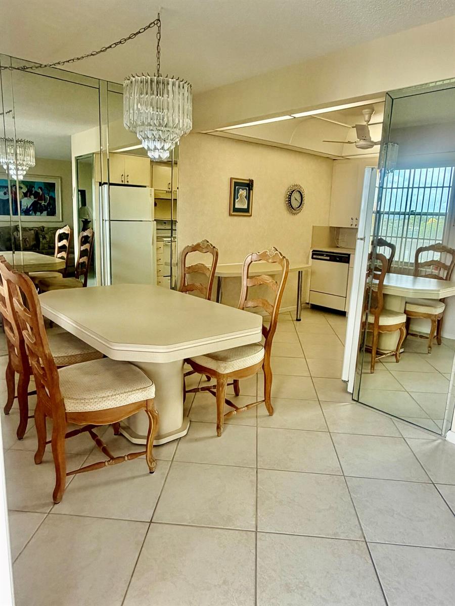 A dining room with a pedestal table, wooden chairs, tiled floors, and mirrored walls — 3035 Rexford, Boca Raton FL 33434, BOCA RATON, FL
