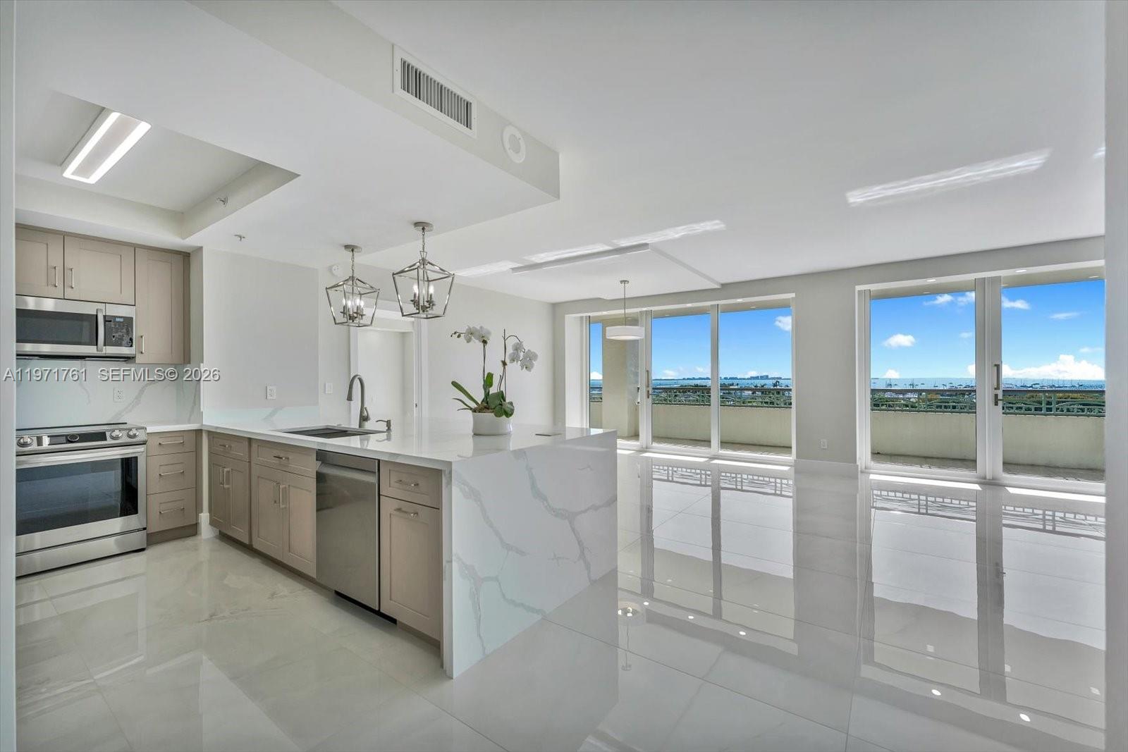 A modern kitchen with light wood cabinets and a marble island overlooks a balcony view — 3400 SW 27th Ave # 602, Miami FL 33133, MIAMI, FL
