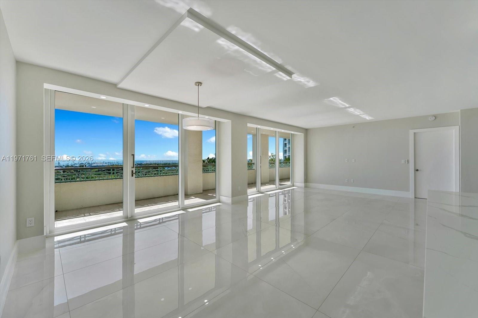 A bright, empty living room features white tile floors, recessed ceiling lighting, and large sliding glass doors — 3400 SW 27th Ave # 602, Miami FL 33133, MIAMI, FL