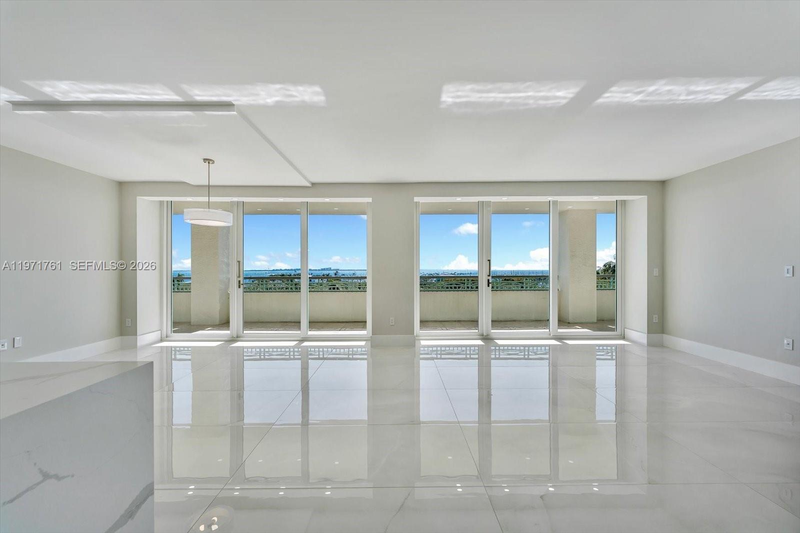 An empty room features white tile floors, recessed lighting, and large glass doors overlooking water — 3400 SW 27th Ave # 602, Miami FL 33133, MIAMI, FL