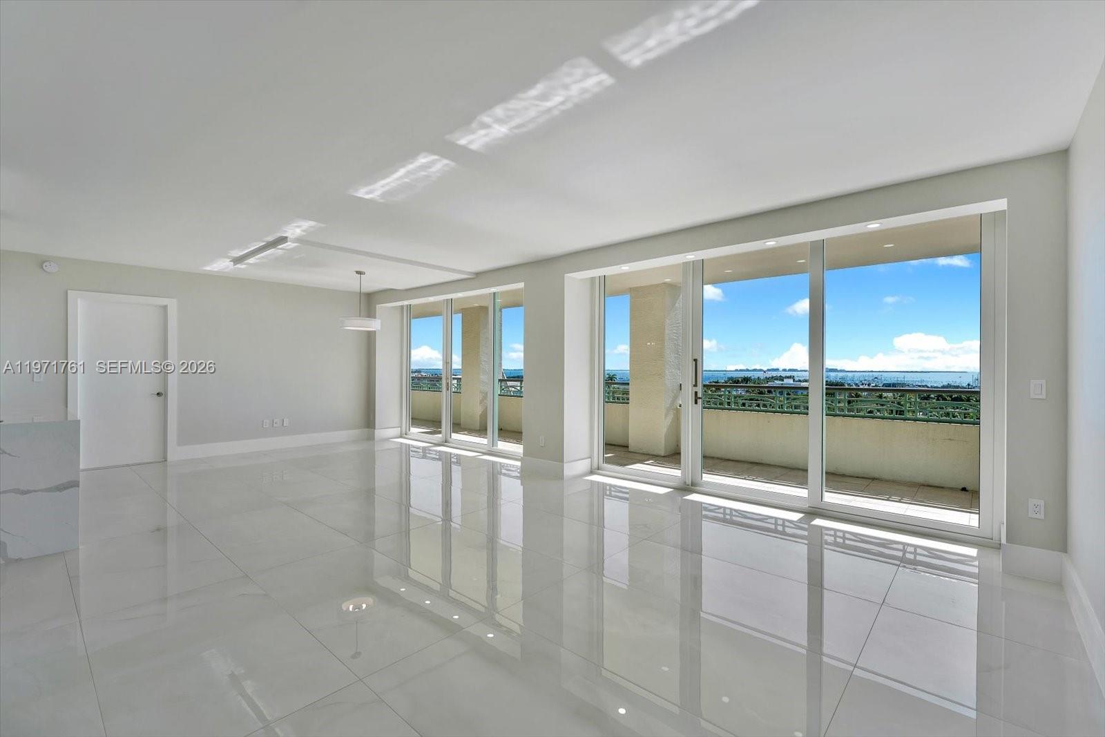 A bright, empty room features white tile flooring, recessed lighting, and large sliding glass doors — 3400 SW 27th Ave # 602, Miami FL 33133, MIAMI, FL