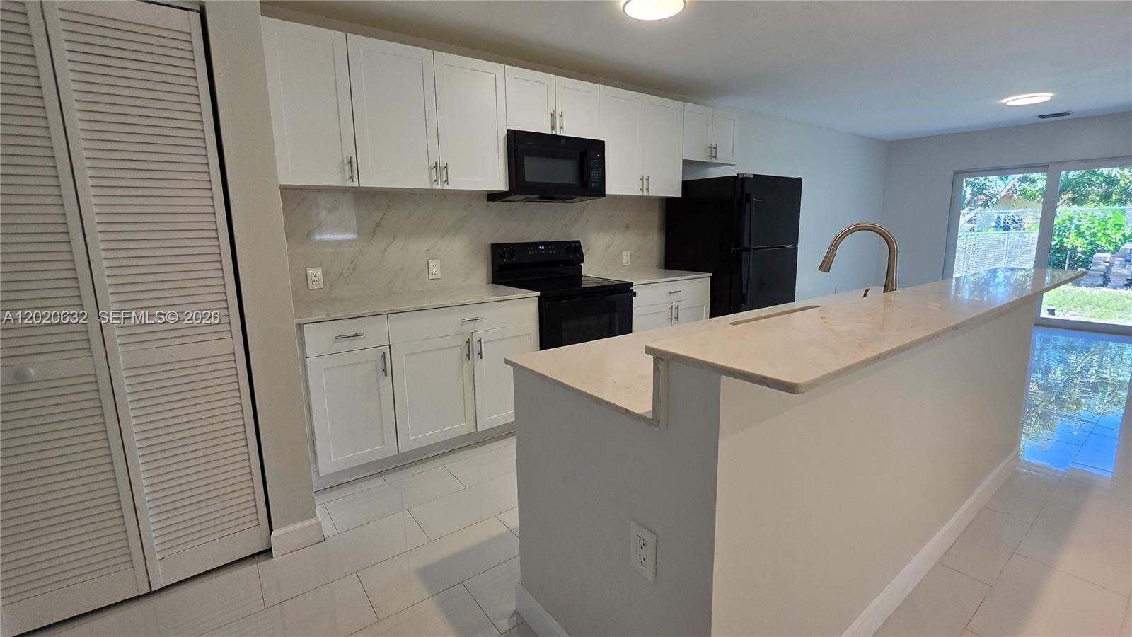 A kitchen features white cabinetry, black appliances, marble-look countertops, and a breakfast bar — 1068 NW 112th St # 1068, Miami FL 33168, MIAMI, FL