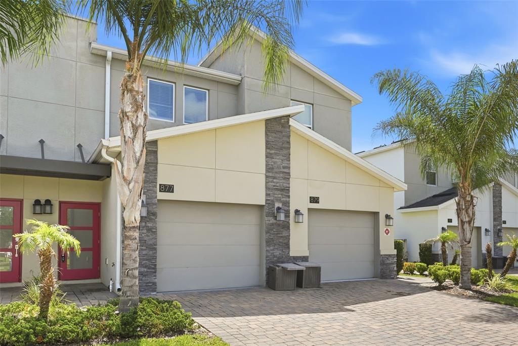 A two-story townhouse exterior features two garage doors, stone accents, and palm trees — 877 OCEAN COURSE AVENUE UNIT 877, DAVENPORT, FL