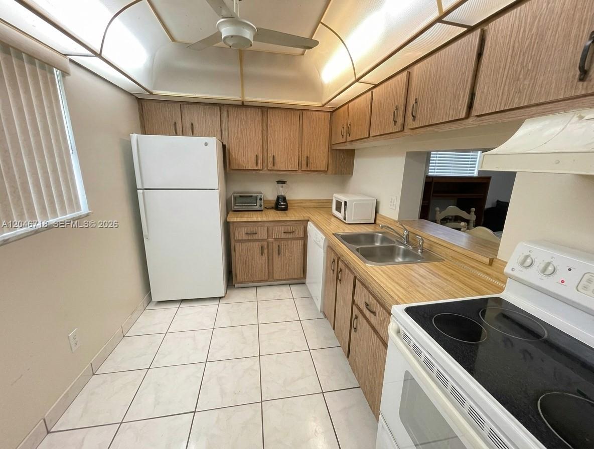 A kitchen features wood cabinets, white appliances, a double sink, and light-colored tile flooring — 2800 NW 56th Ave # B207, Lauderhill FL 33313, LAUDERHILL, FL