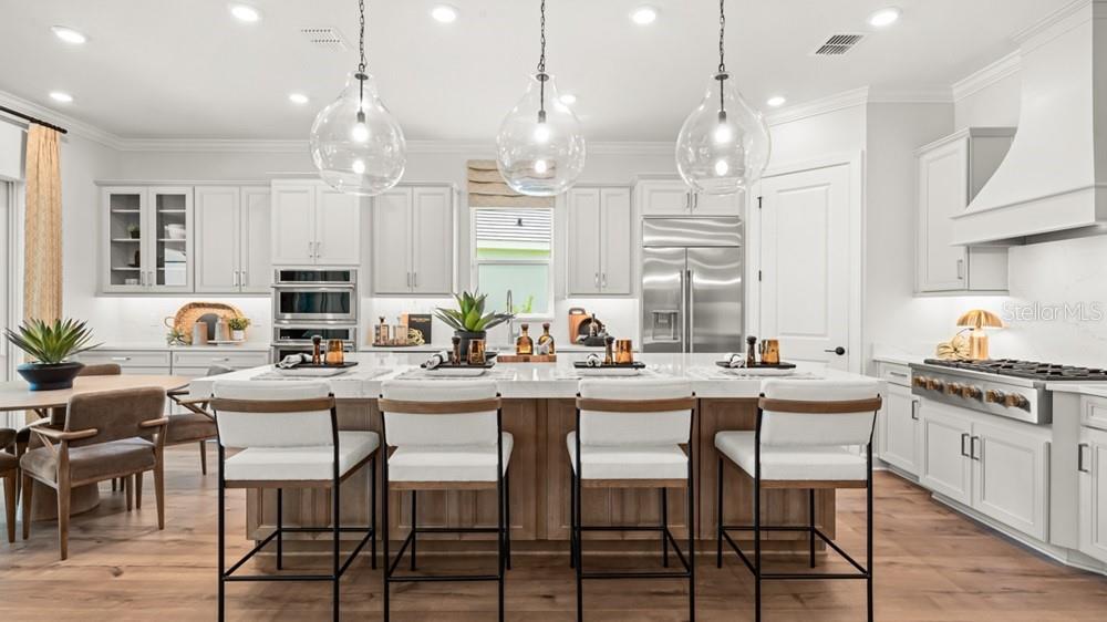 A modern kitchen features a large island with four stools, white cabinetry, and pendant lighting — 26112 ASPARANO AVENUE, ENGLEWOOD, FL