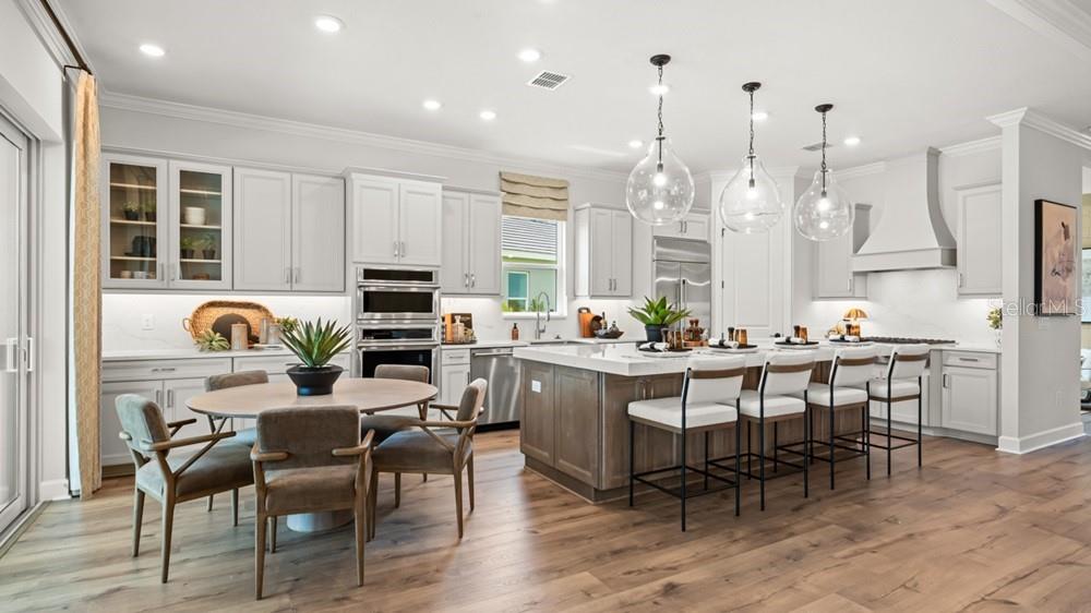 A modern kitchen features light gray cabinetry, a wood-toned island, and a round dining table — 26112 ASPARANO AVENUE, ENGLEWOOD, FL